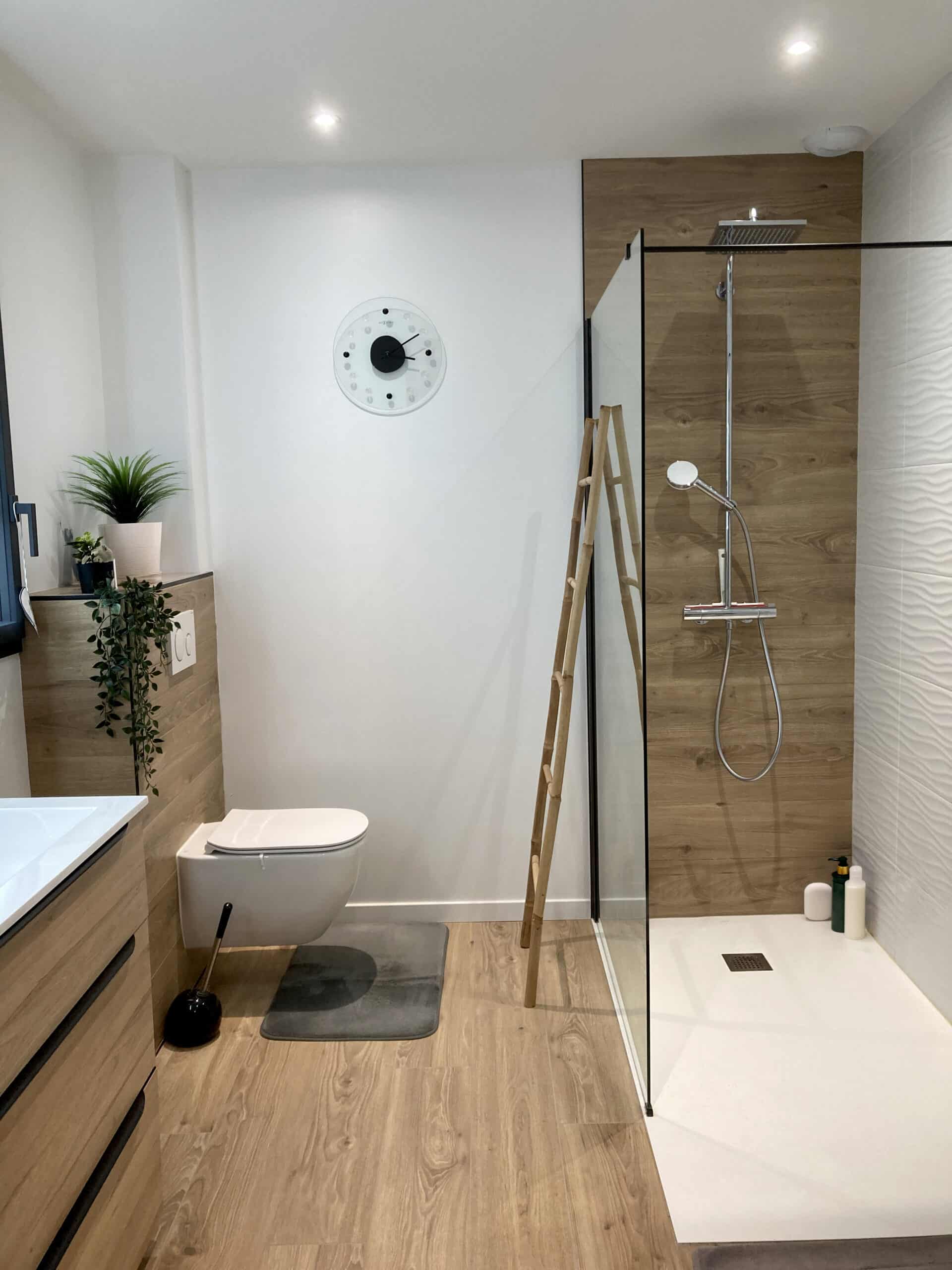 Salle de bain moderne avec WC suspendu, vasque en bois clair, douche à l'italienne avec mur imitation bois et horloge murale Nixón.